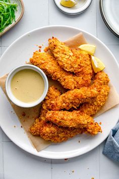 fried chicken on a plate with dipping sauce and lemon wedges next to the side