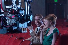 a man and woman sitting on red chairs in front of a movie projector smiling at each other