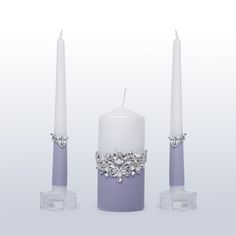 three white candles with crystal decorations on each candle holder, one in purple and the other in silver