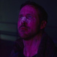 a man with blue eyes stares into the distance while standing in a dark room at night