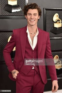 a young man in a red suit and white shirt smiles for the camera on the red carpet