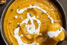 a metal bowl filled with carrot soup and sour cream on top of a wooden table