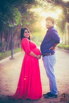 a pregnant woman and man standing next to each other in front of trees at sunset