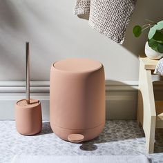 a pink stool next to a white towel and potted plant in a room with beige walls