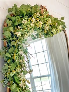 a mirror hanging on the wall with flowers and greenery in it's frame