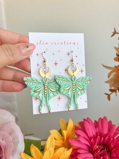 a pair of green and gold earrings on a card with flowers in the foreground