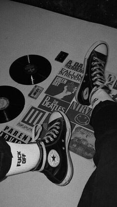 black and white photograph of someone's feet with their shoes on top of records