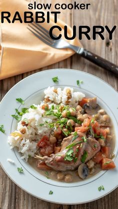 a white plate topped with meat and rice next to a fork on a wooden table