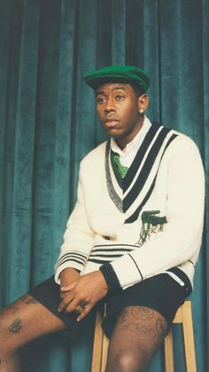 a man sitting on top of a wooden chair wearing a green hat and sweater over his shoulder