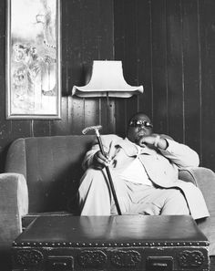 a black and white photo of a man sitting on a couch with a cane in his hand