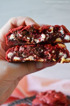 two red velvet cookies with white chocolate and marshmallows are in someone's hand