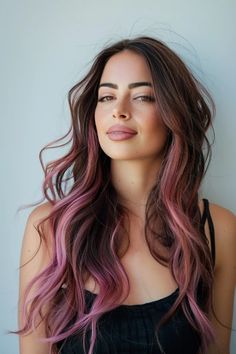 Woman with long, wavy hair dyed in shades of brown and pink, wearing a black top against a plain background. Pink Hair On Brunette Dark Brown, Pink Lowlights In Black Hair, Dark Brown Hair With Rose Gold Money Piece, Hint Of Pink Hair, Dark Hair Color With Money Piece, Black Hair With Rose Gold Money Piece, Dusty Pink Ombre Hair, Rose Gold Highlights Brunette Dark Brown Balayage Hair, Brunette Hair With Peekaboo Color