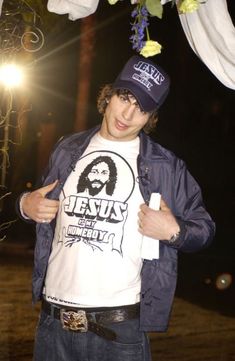 a young man wearing a jesus t - shirt under a canopy with flowers hanging from it