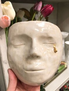 a person holding up a white ceramic face