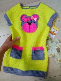 someone is holding up a yellow sweater with pink and grey bear on the front that has been crocheted