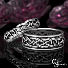 two silver rings sitting next to each other on top of a black surface with pink flowers in the background