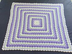 a crocheted blanket is laying on a black tablecloth with purple and green squares