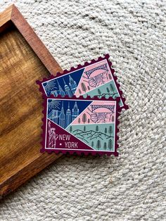 two new york stamps sitting on top of a wooden cutting board next to a piece of wood