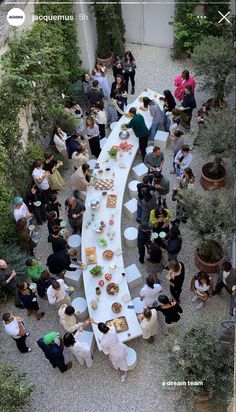 a group of people standing around a long table with food on it in an outdoor courtyard