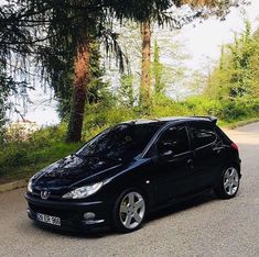 a black car is parked on the side of the road near some trees and bushes