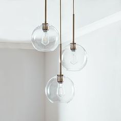 three clear glass globe pendant lights hanging from a ceiling fixture in a white walled room