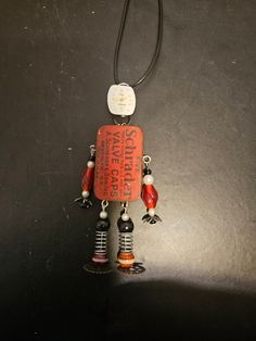 a necklace with an orange and black robot charm hanging from it's side on a black surface