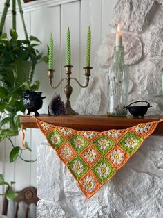 an orange and green crocheted triangle hanging from a mantle with candles on it