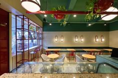 an empty restaurant with tables and chairs in front of the window, along with plants hanging from the ceiling