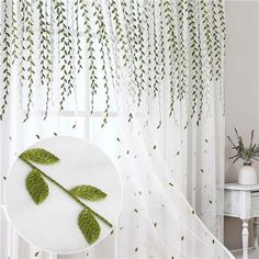 two green leaves are hanging on the curtain in front of a white table and chair