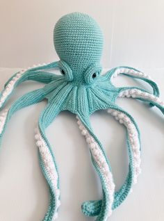 an octopus crocheted in teal and white sits on a bed with its head turned to the side