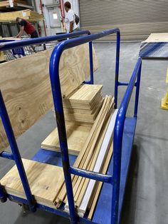 several pieces of wood on a blue dolly in a warehouse with two men working behind them