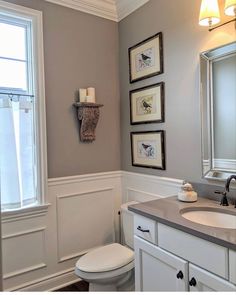 a white toilet sitting next to a sink in a bathroom under two framed pictures on the wall