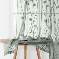 a table with a bowl on top of it next to a window covered in sheer curtains