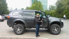 a woman standing in the drivers seat of a gray four - doored suv with her cell phone to her ear