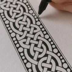 a person writing on paper with a pen in their left hand and an intricate design