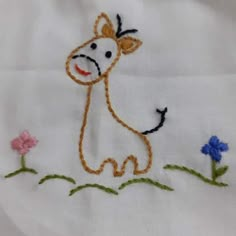 a small embroidered cow sitting in the grass on a white cloth with blue and pink flowers