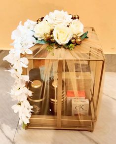 a gold box with white flowers and perfume bottles in it on the floor next to a wall