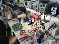 many electronic devices and wires on a table in a room with lots of clutter