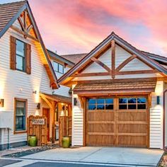 a white house with wooden garage doors and windows in front of a pink sky at sunset