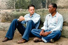 two men sitting next to each other in front of a stone wall with an advertisement on it