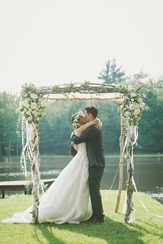 a bride and groom kissing under an arch made out of branches with flowers on it