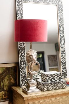 a red lamp sitting on top of a wooden table next to a mirror and box