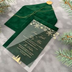 two green envelopes with gold foil and snowflakes on them next to evergreen branches