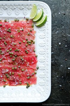 watermelon and capers on a white plate with lime wedges