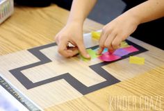 a child is playing with colored paper on a wooden table and cutting it into squares