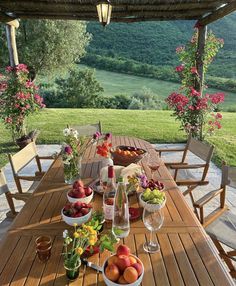 a wooden table topped with bowls of fruit next to a lush green hillside covered in flowers