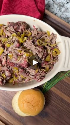 a white bowl filled with meat and vegetables on top of a wooden cutting board next to bread