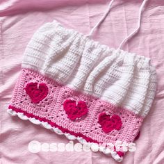 a crocheted pink and white purse with hearts on it sitting on a bed