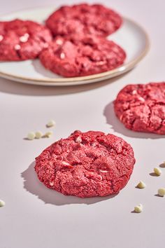 three red cookies on a white plate next to two plates with one cookie and the other is half eaten