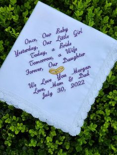 a white handkerchief with embroidered words on it sitting in some green bushes and grass,